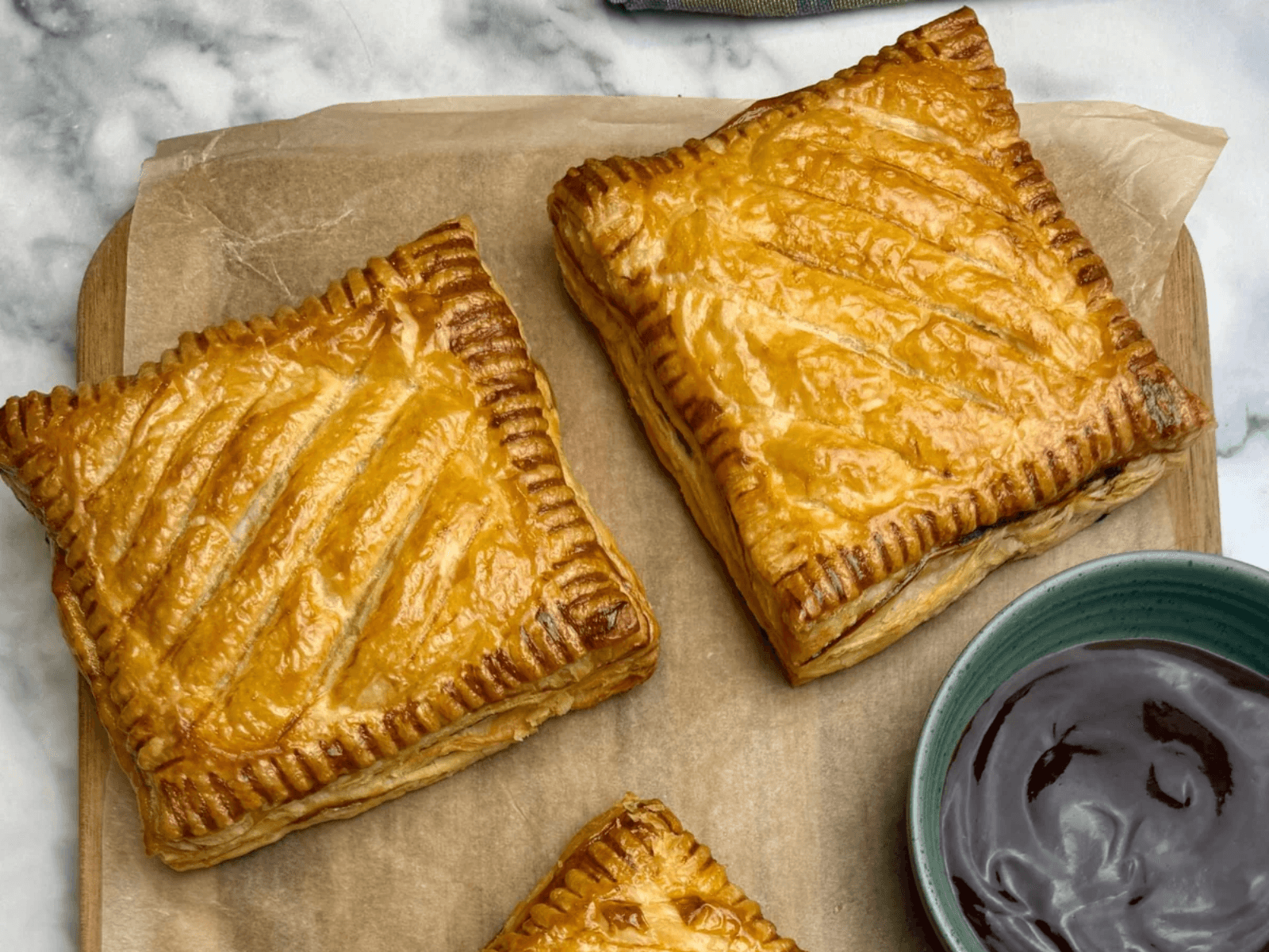 Homemade Greggs steak bakes with golden puff pastry served on baking paper with dipping sauce