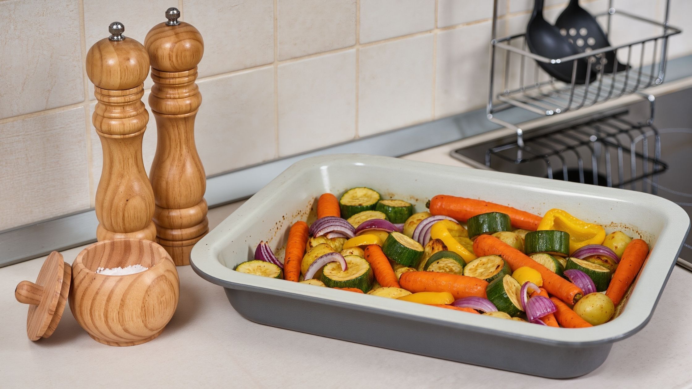 Sea salt and grinder on kitchen counter next to roasted veg.