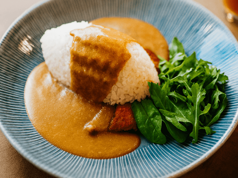 Chicken katsu curry with rice, curry sauce and salad on a blue plate.