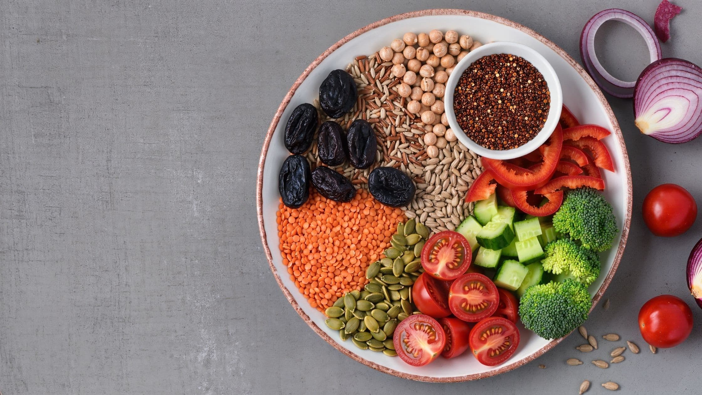 An overhead shot of a bowl of mixed legumes, whole grains, prunes, seeds, and fresh vegetables.