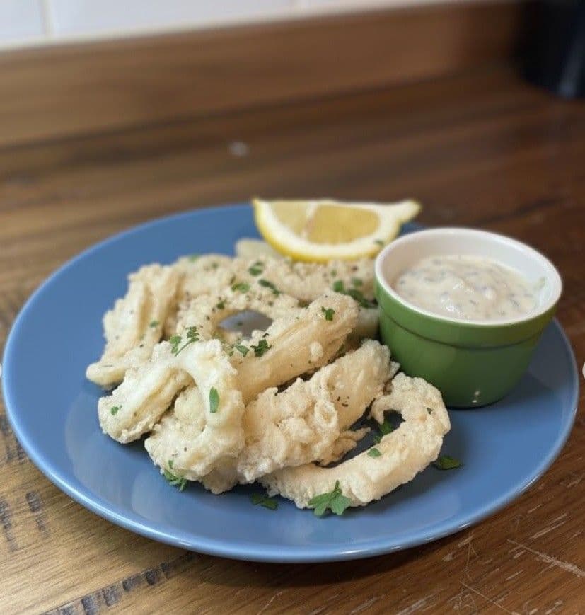 Crispy fried calamari rings with a lemon wedge and a side of tartar sauce on a blue plate set on a wooden surface.