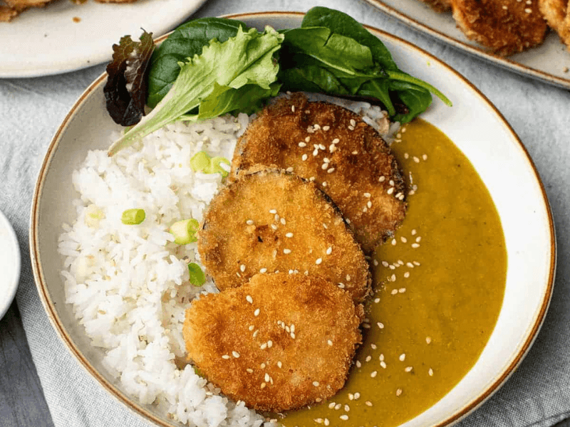 Homemade Wagamama Yasai Katsu Curry with breaded aubergine slices, curry sauce, rice, and salad leaves
